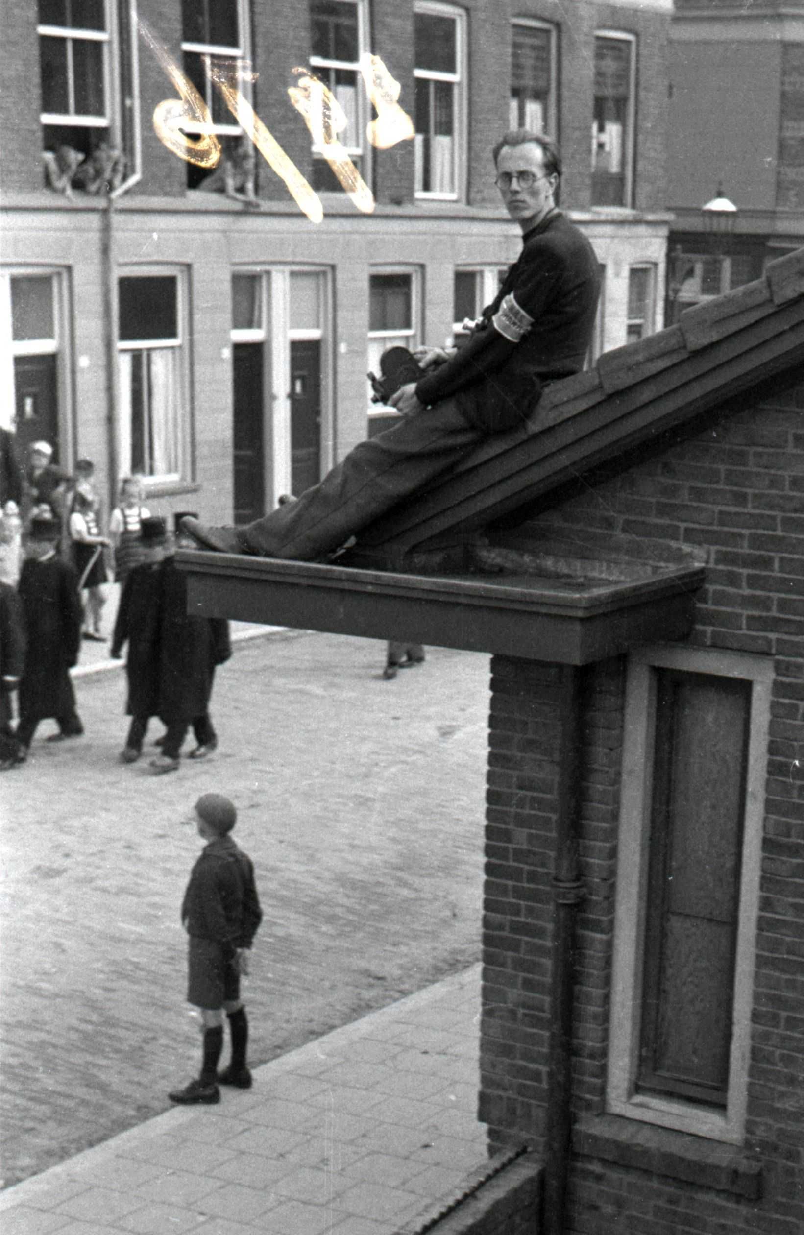 Leen Timp zit in de dakrand om de uitvaart van twee omgekomen BS-leden vast te leggen, mei 1945. (NIOD 187553)