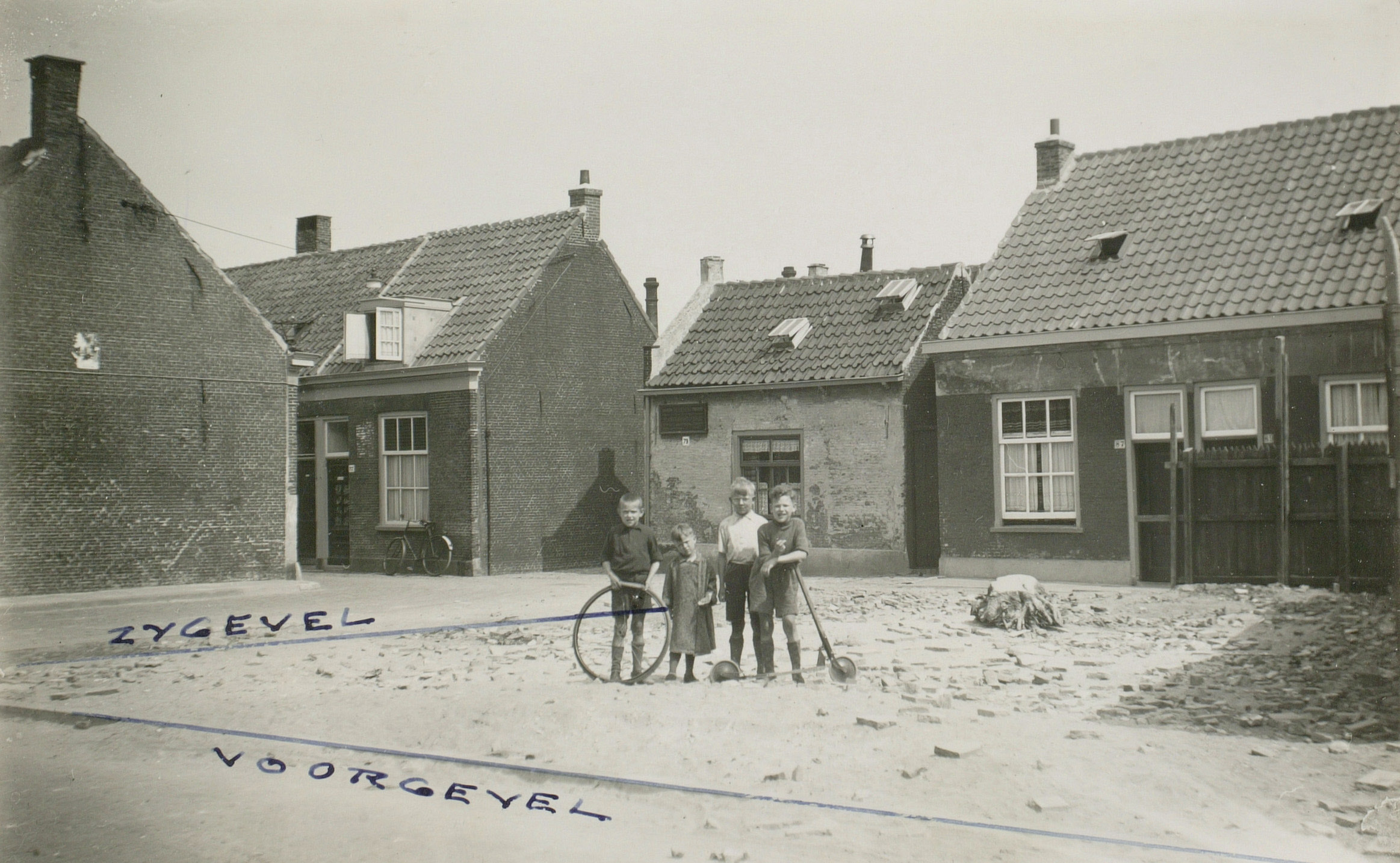 Een oude zwart-wit foto van kinderen die voor oude arbeiderswoningen staan.