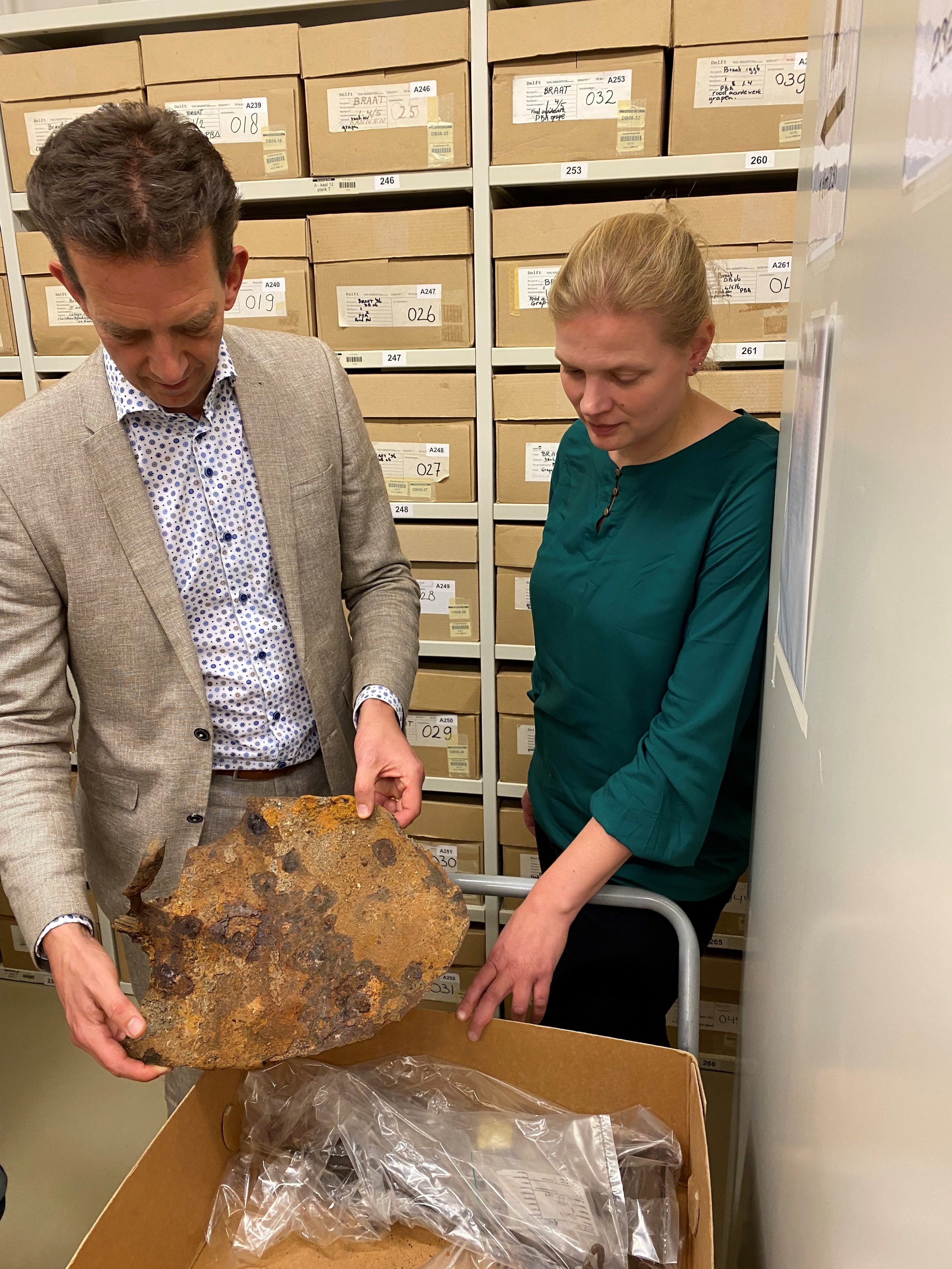 Man toont een verroeste bodemvondst in een archeologisch depot met een vrouwelijke collega ernaast.